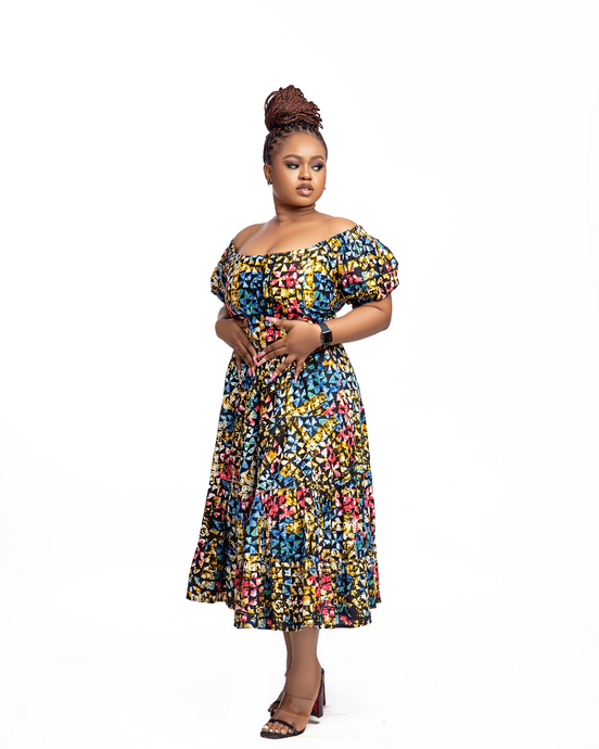 Heba is an off-shoulder African print (Ankara) midi dress with an elasticized puffed sleeve, a fitted bodice, tie-back details, and gathers beneath. She comes with pockets.  The model is wearing a size 14.